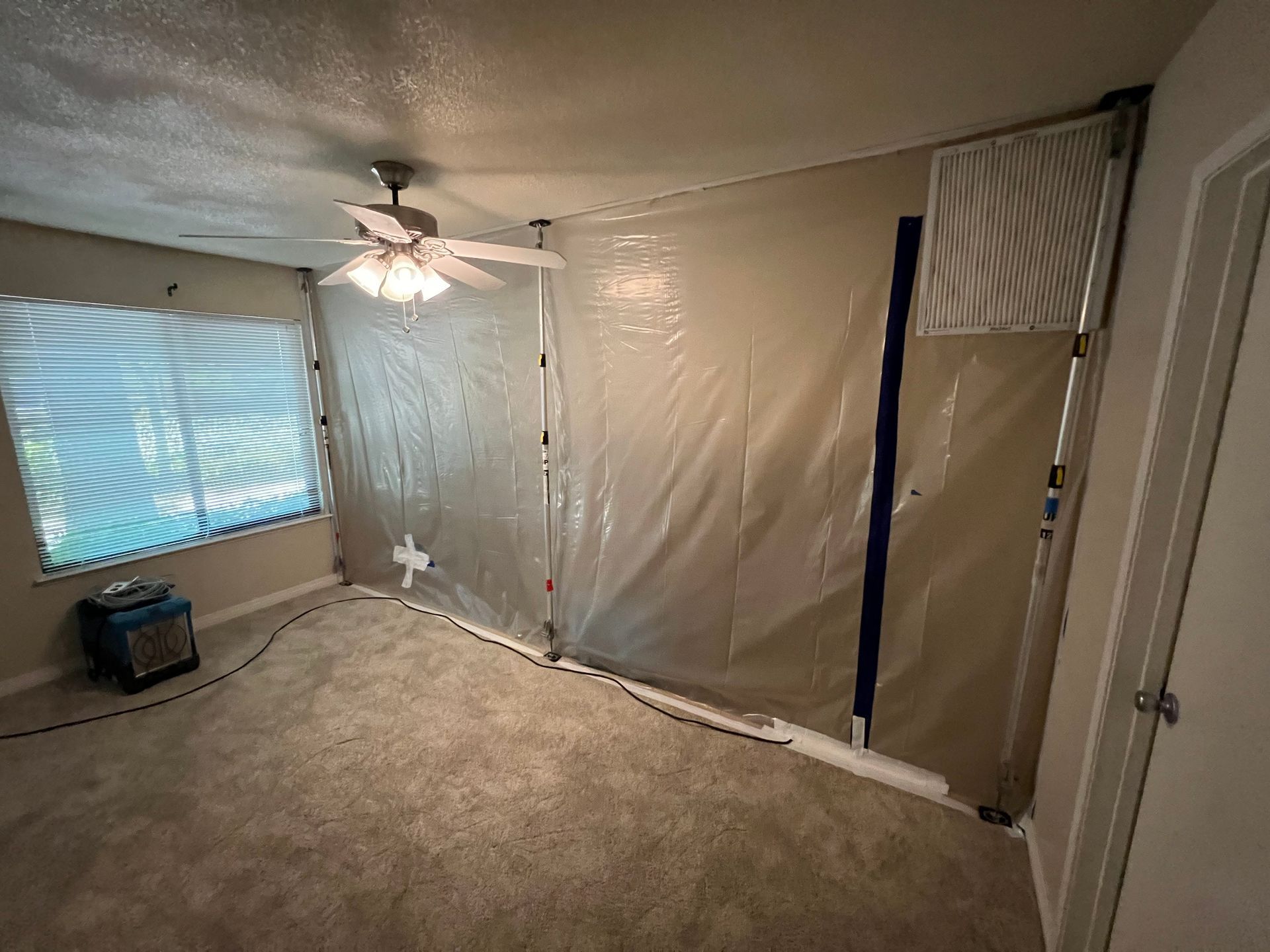 A room with a ceiling fan and a plastic tarp on the wall.