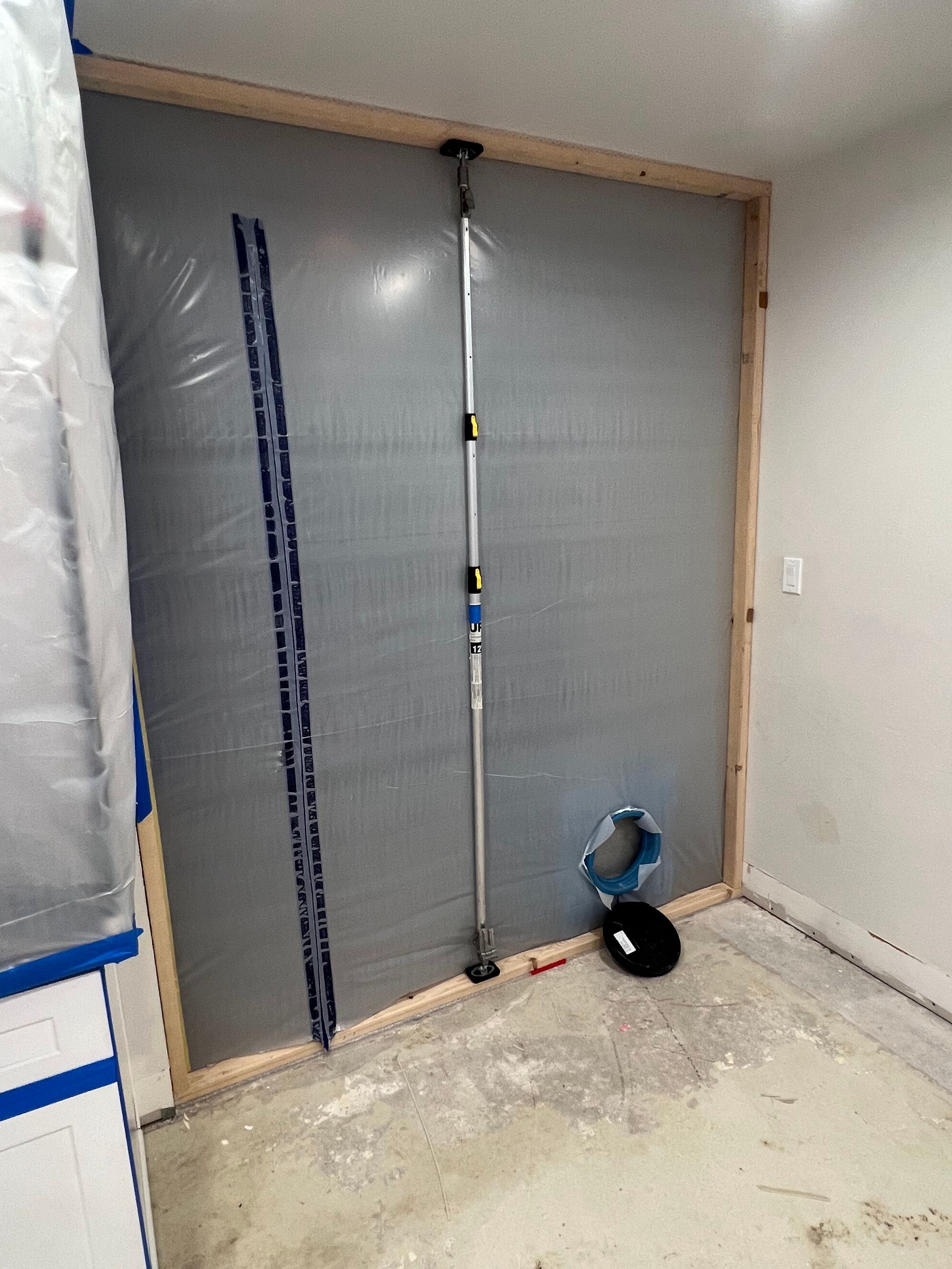 A room with a wall covered in plastic and a fan on the floor.