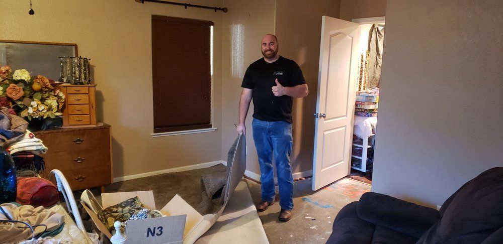 A man is standing in a living room holding a piece of wood and giving a thumbs up.