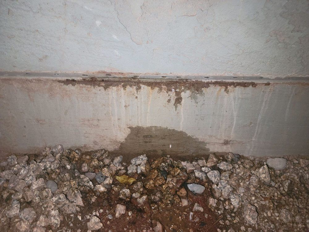 A concrete wall with a lot of rocks on the ground underneath it.