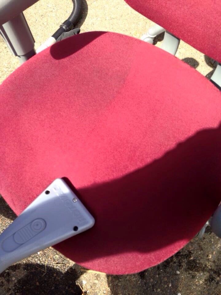 A red chair is being cleaned with a vacuum cleaner.