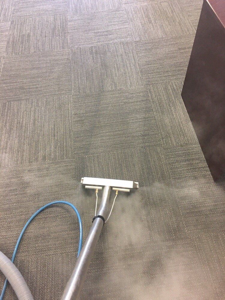A vacuum cleaner is cleaning a carpeted floor in an office.