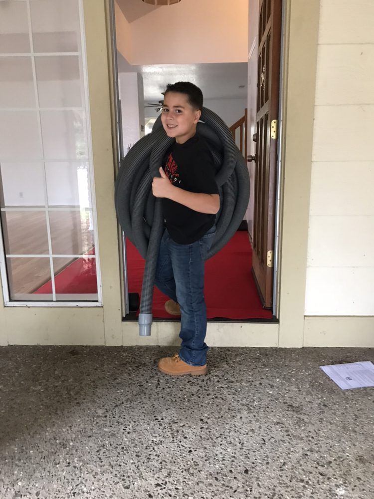 A young boy is holding a large hose in front of a door
