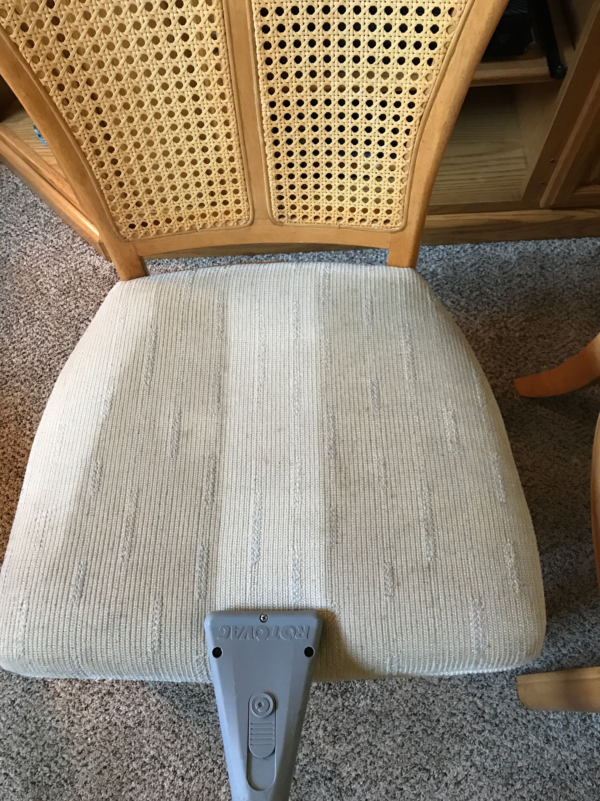A chair with a wicker back is being cleaned with a vacuum cleaner.