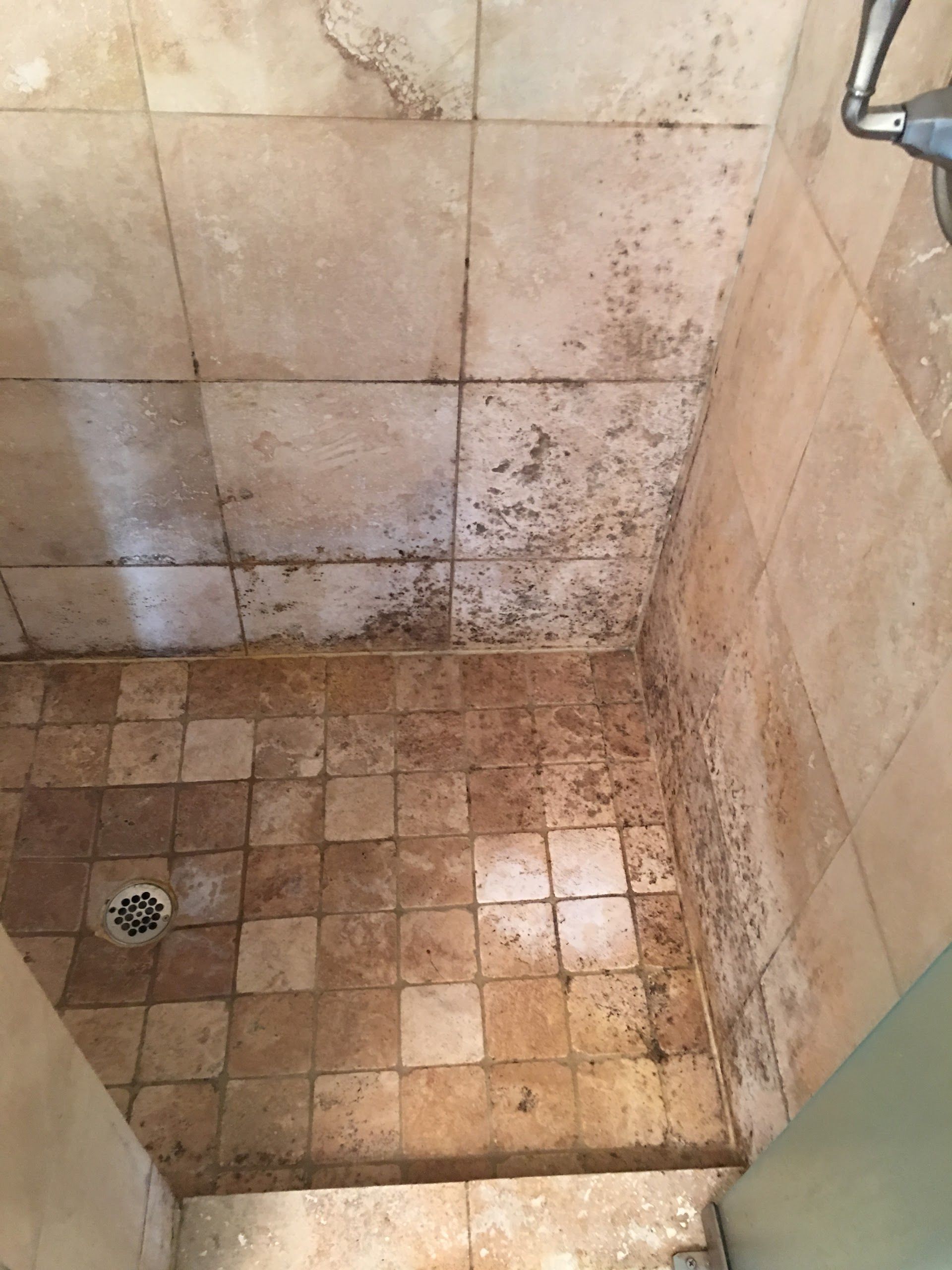 A shower stall with dirty tiles and a drain.