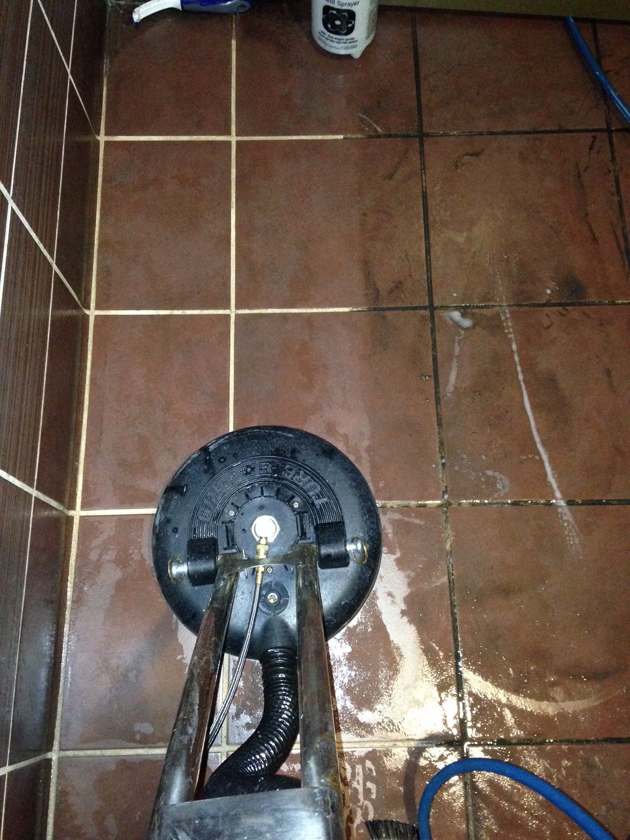 A vacuum cleaner is sitting on a tiled floor next to a hose.