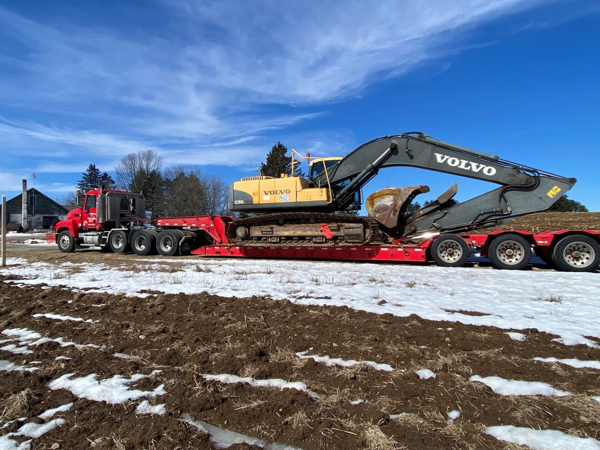 Red semi-truck hauling a yellow Volvo excavator