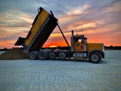 Yellow dump truck unloading gravel at sunset