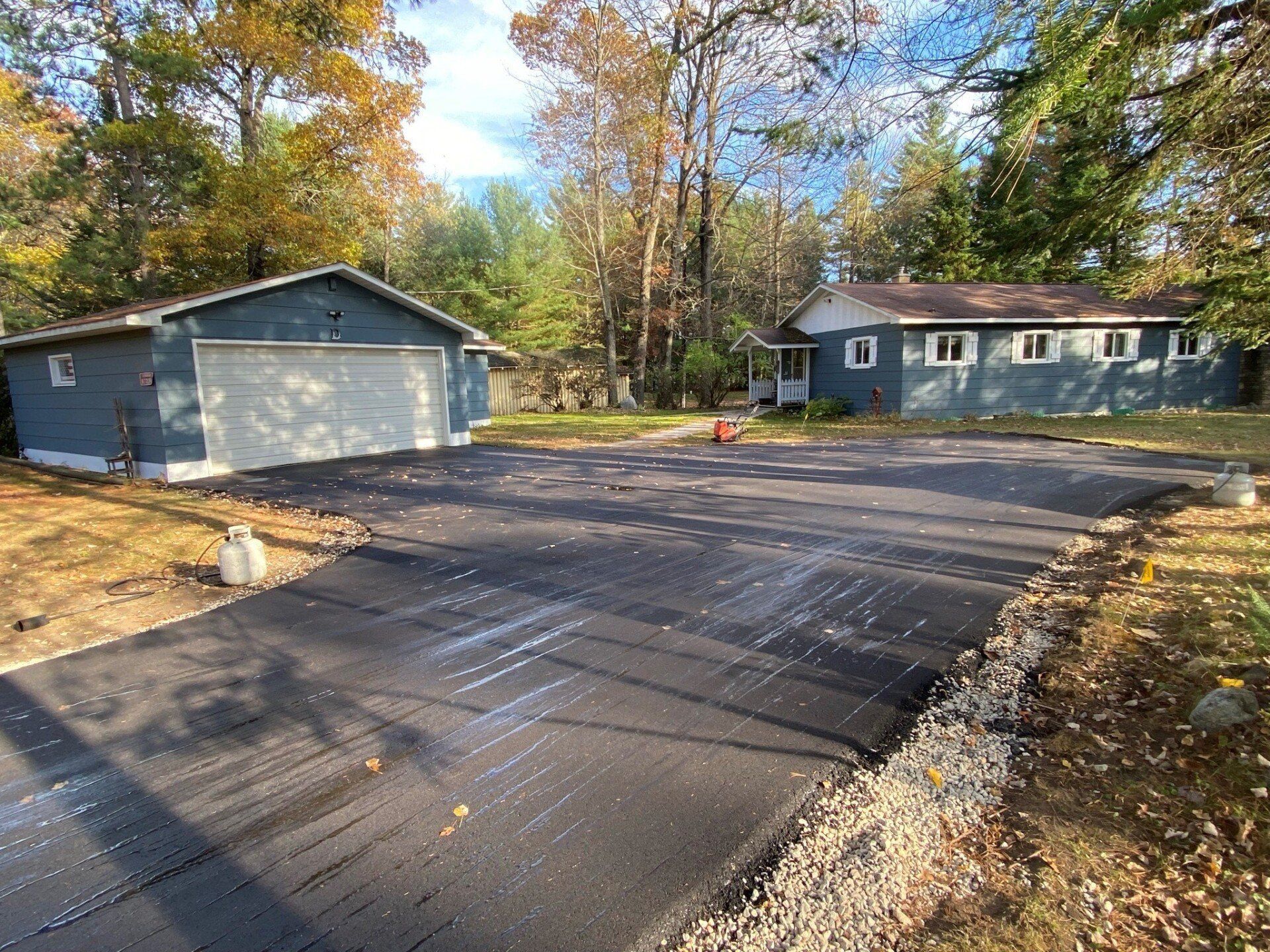 Newly paved driveway in front of two blue buildings and fall trees