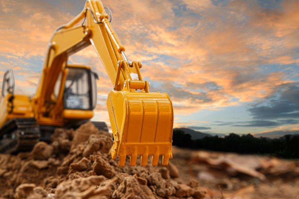 Yellow excavator digging earth under a colorful sunset sky
