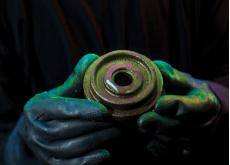 A person wearing black gloves is holding a piece of metal