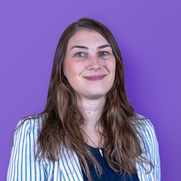 Woman with long brown hair and a striped jacket smiles against a purple background.