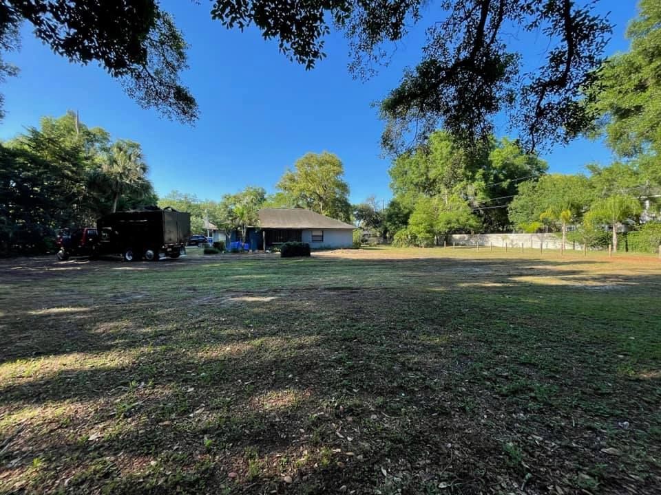 A large grassy field with a house in the background and trees in the foreground.