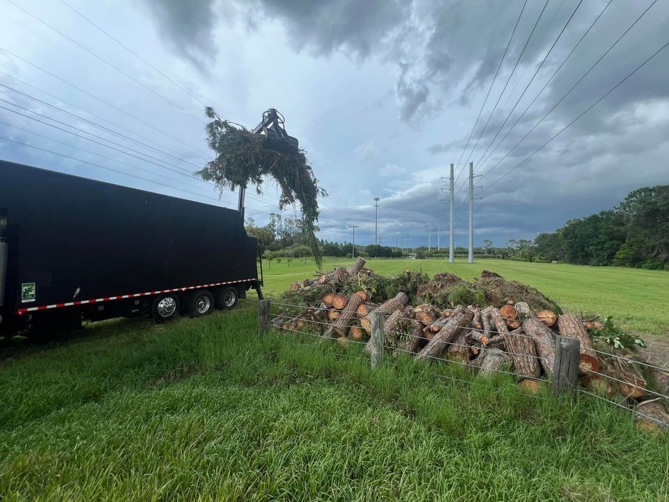 A truck is parked next to a pile of logs in a field.