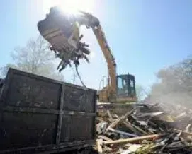 Excavator loading debris into a dumpster on a sunny day.