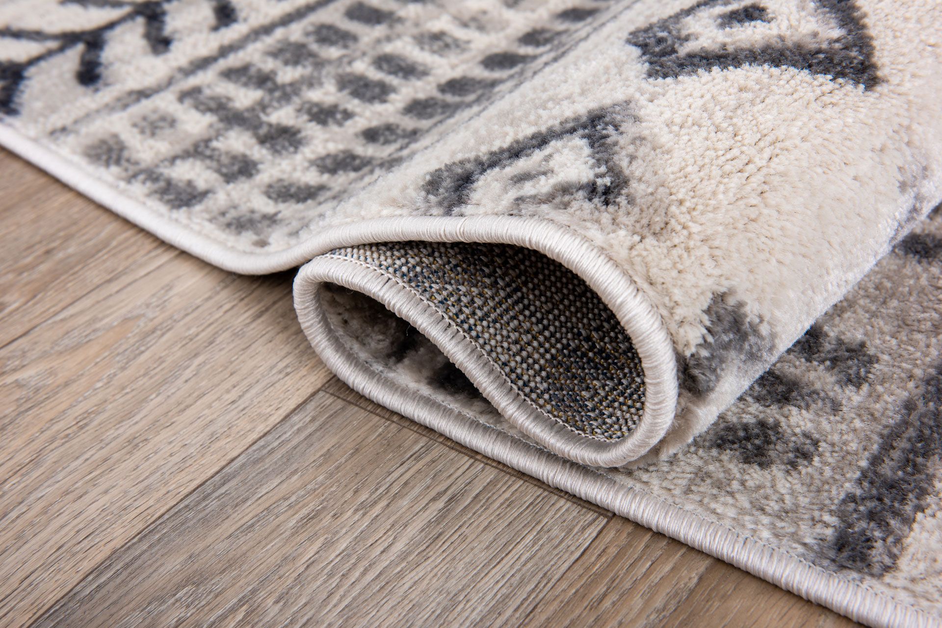 Rolled up beige and gray patterned rug on a wooden floor.