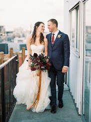 A bride and groom are walking down a balcony holding hands and looking at each other.