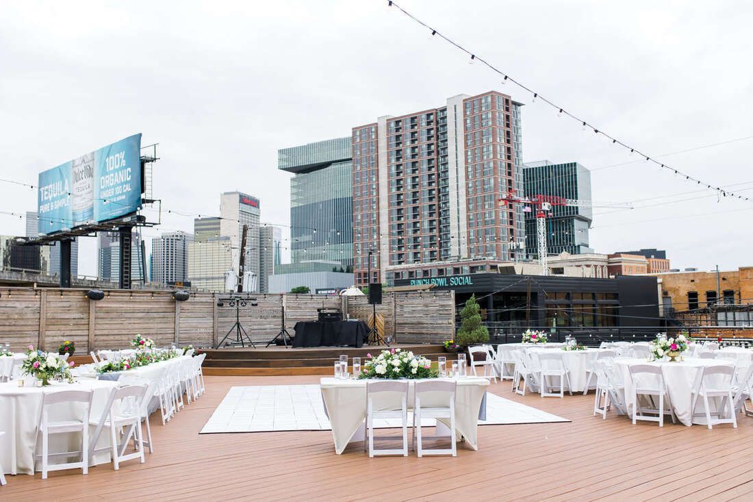 A patio with tables and chairs set up for a wedding reception with a city skyline in the background.