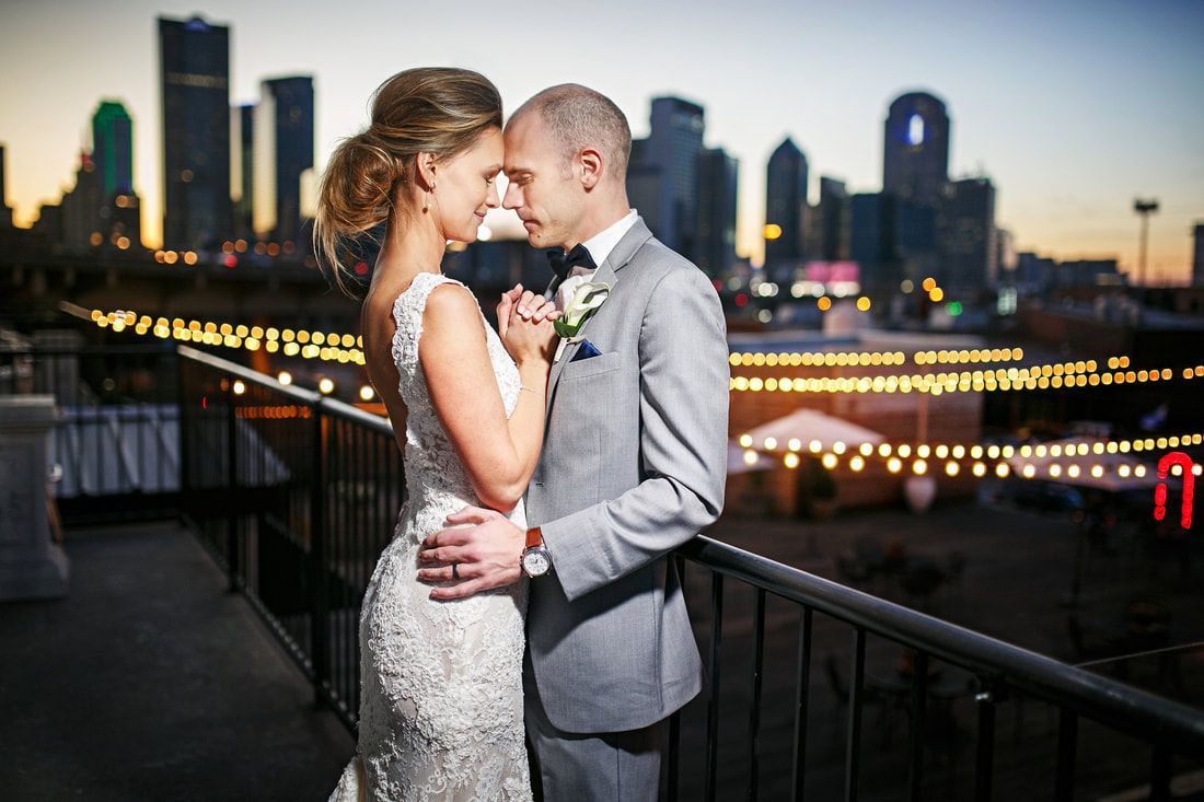 A bride and groom are posing for a picture on a balcony with a city skyline in the background.