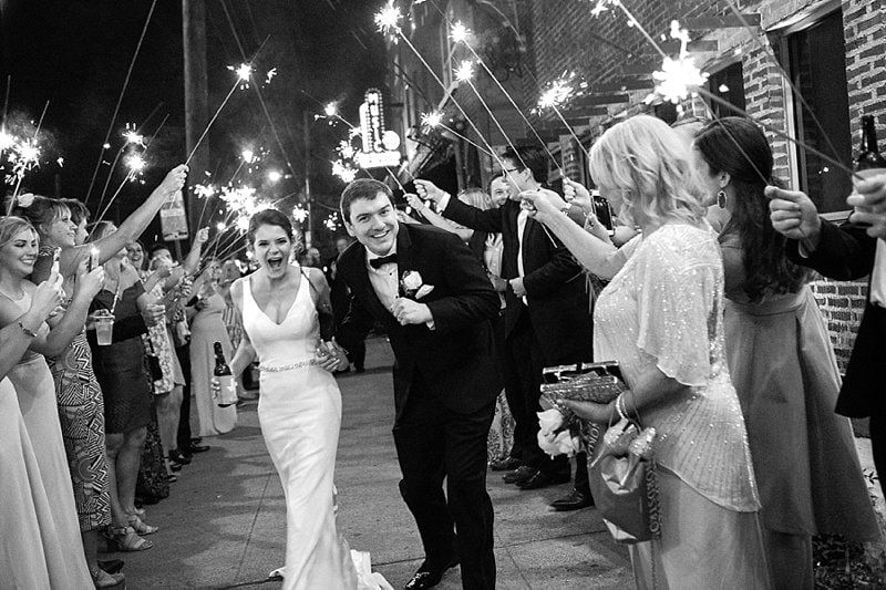 A bride and groom are walking through a crowd of people holding sparklers.