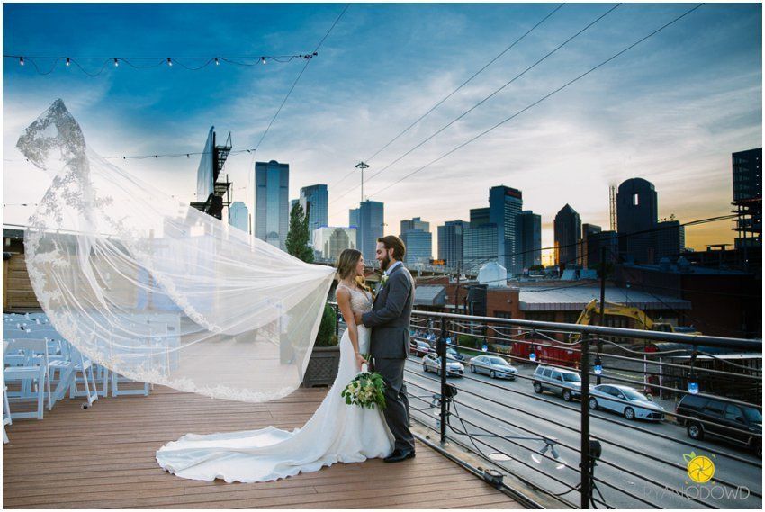 A bride and groom are posing for a picture on a balcony with a city skyline in the background.