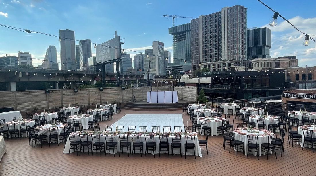 A large patio with tables and chairs set up for a wedding reception with a city skyline in the background.