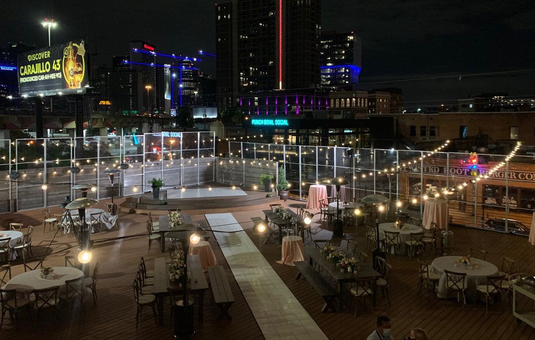 A large patio area with tables and chairs at night with a city in the background.