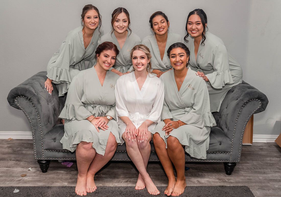 A bride and her bridesmaids are posing for a picture while sitting on a couch.