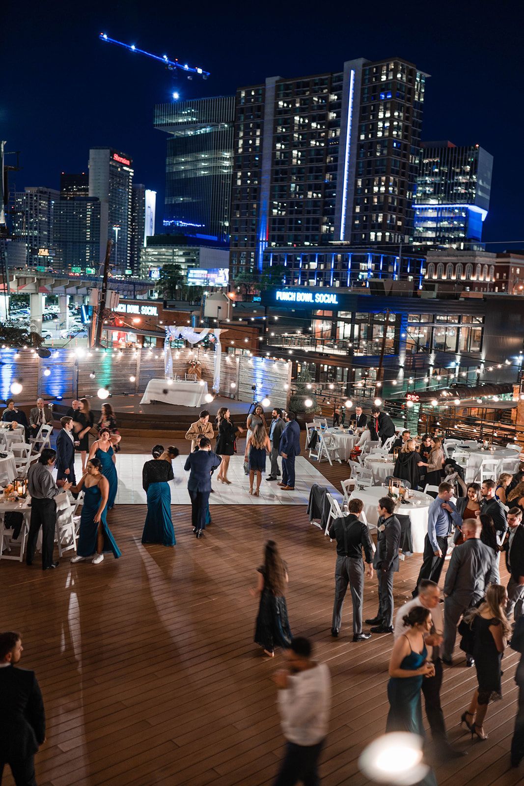 A group of people are dancing on a wooden floor in front of a city skyline at night.
