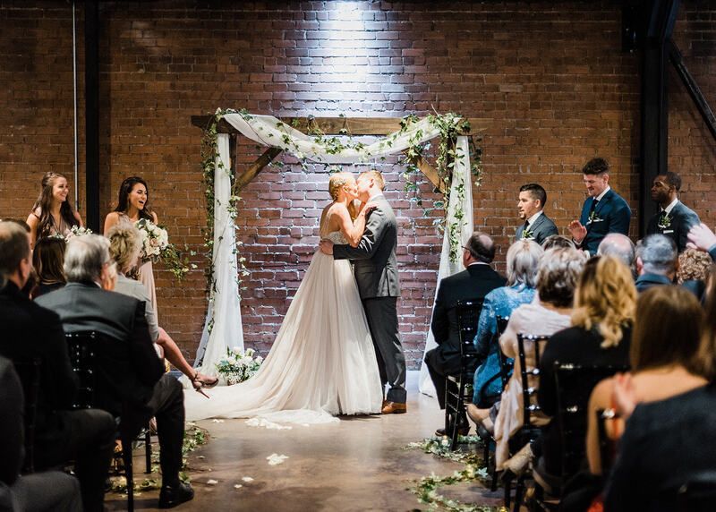 A bride and groom are kissing during their wedding ceremony in front of their wedding guests.