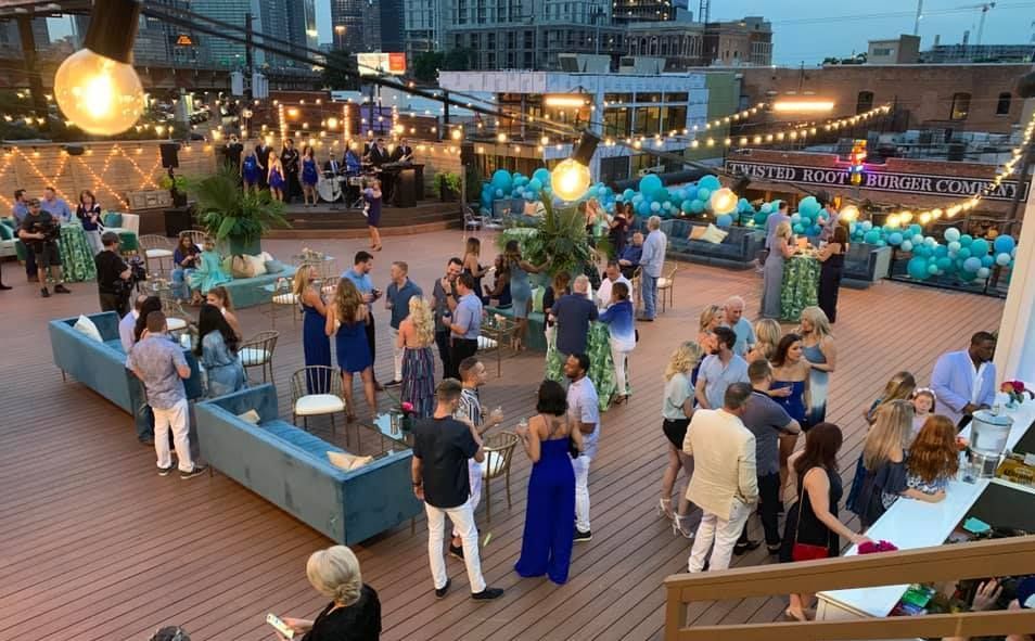 A large group of people are standing on a rooftop deck.
