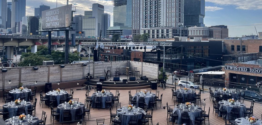 A patio with tables and chairs set up for a wedding reception with a city skyline in the background.