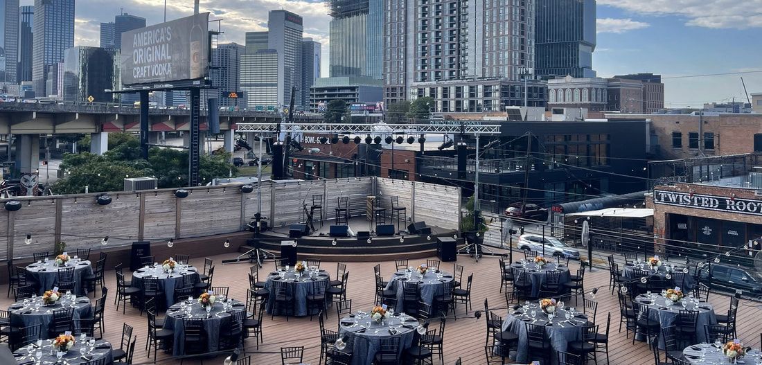 A large group of tables and chairs are set up in front of a city skyline.