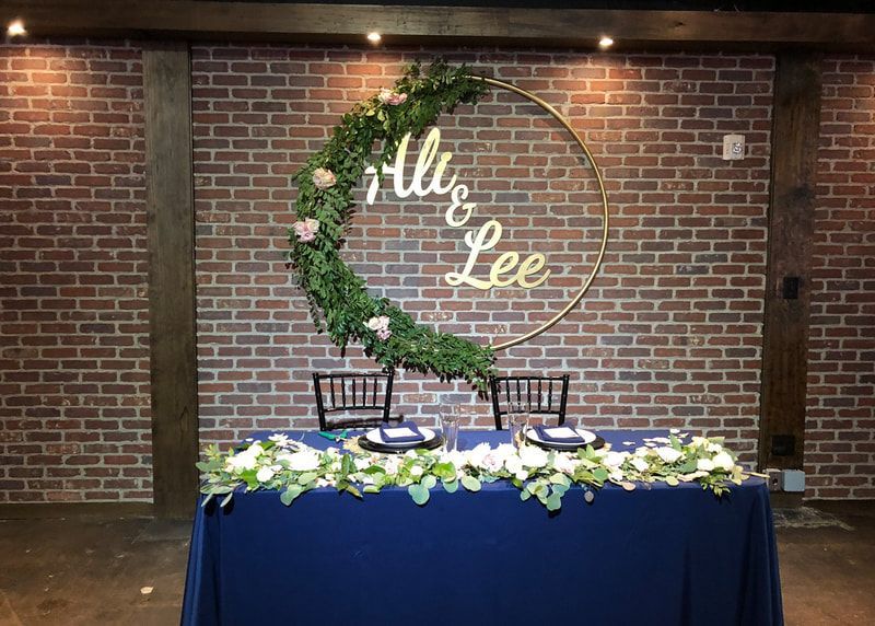 A table with a blue tablecloth is in front of a brick wall.