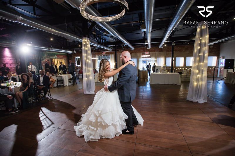 A bride and groom are dancing in a large room at their wedding reception.