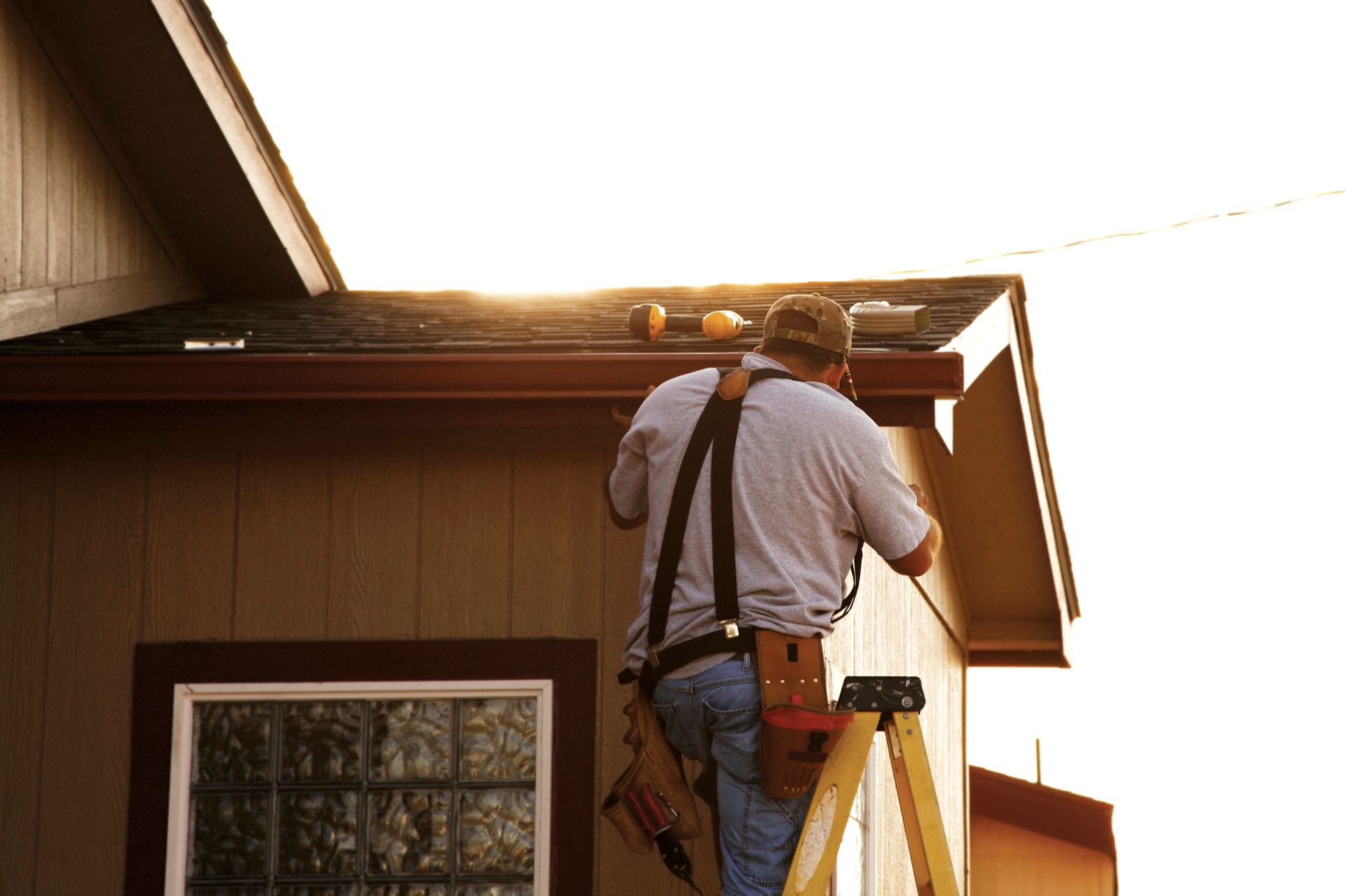 Person on ladder installing gutter on house roof.