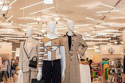 Three mannequins wearing clothing in a store. Overhead lights illuminate the setting.
