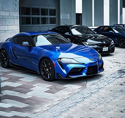 Blue sports car parked in front of garage with three black and blue cars behind it.