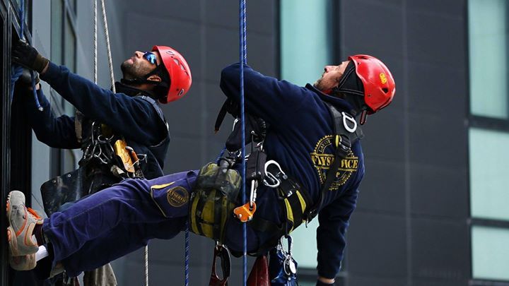 Due persone con imbracature e caschi si calano in corda doppia dall'esterno di un edificio.