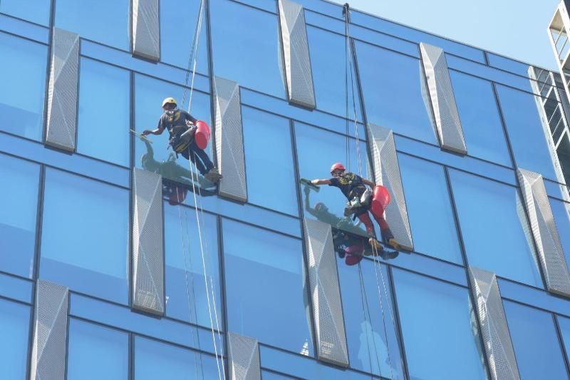 Due lavavetri sospesi su delle corde puliscono le finestre di un moderno edificio per uffici.