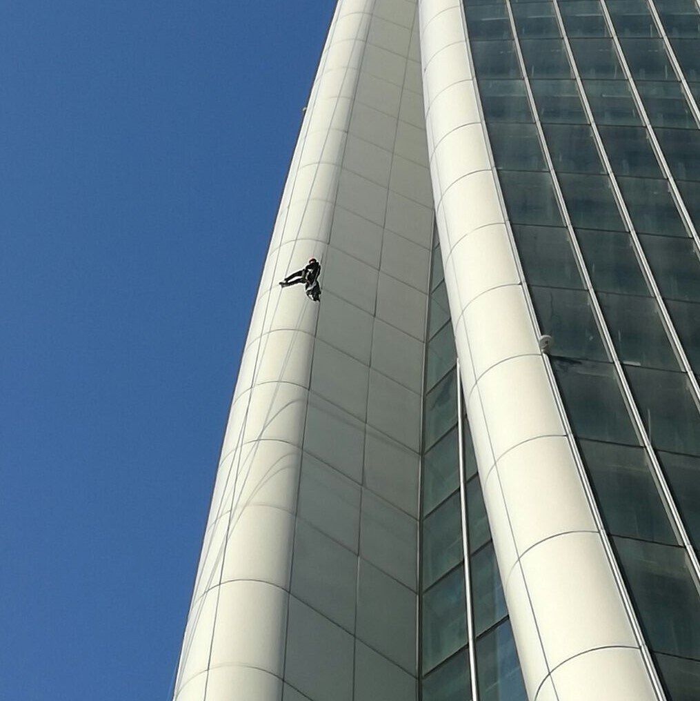 Un lavavetri sospeso su un alto grattacielo bianco contro un cielo azzurro e terso.