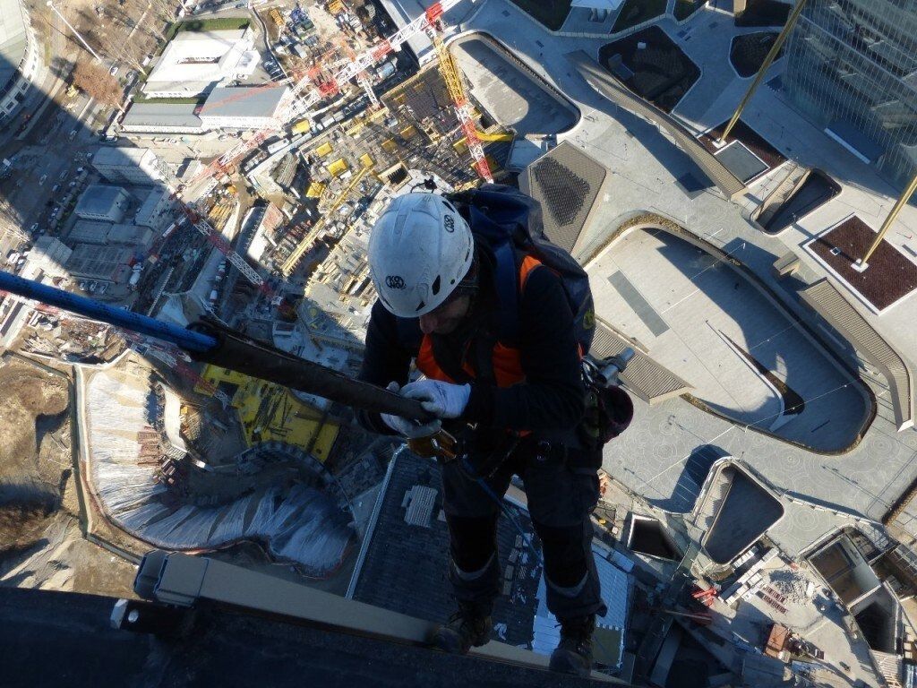 Persona che si cala in corda doppia da un edificio alto, assicurata da corde e con indosso un casco. Vista dall'alto.