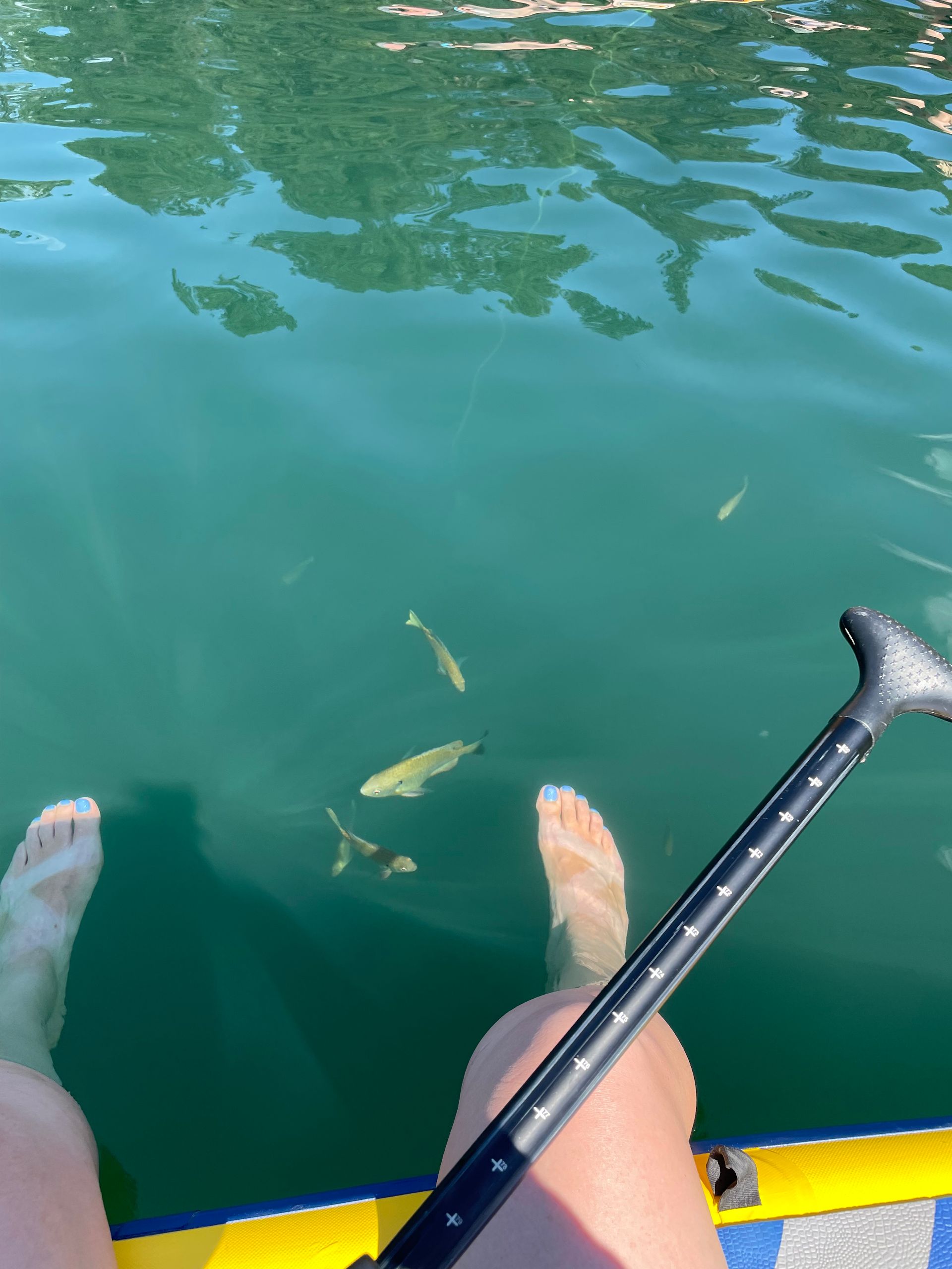 A person is sitting on a paddle board in the water with their feet in the water.
