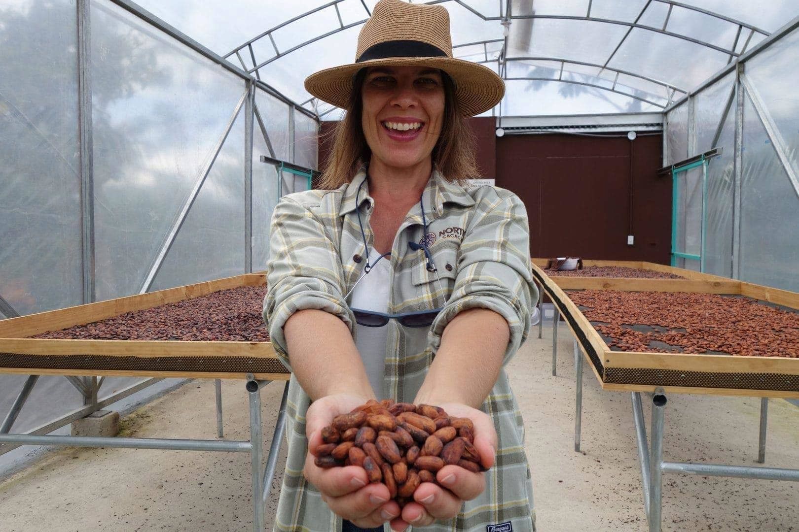A woman in a hat is holding beans in her hands in a greenhouse.