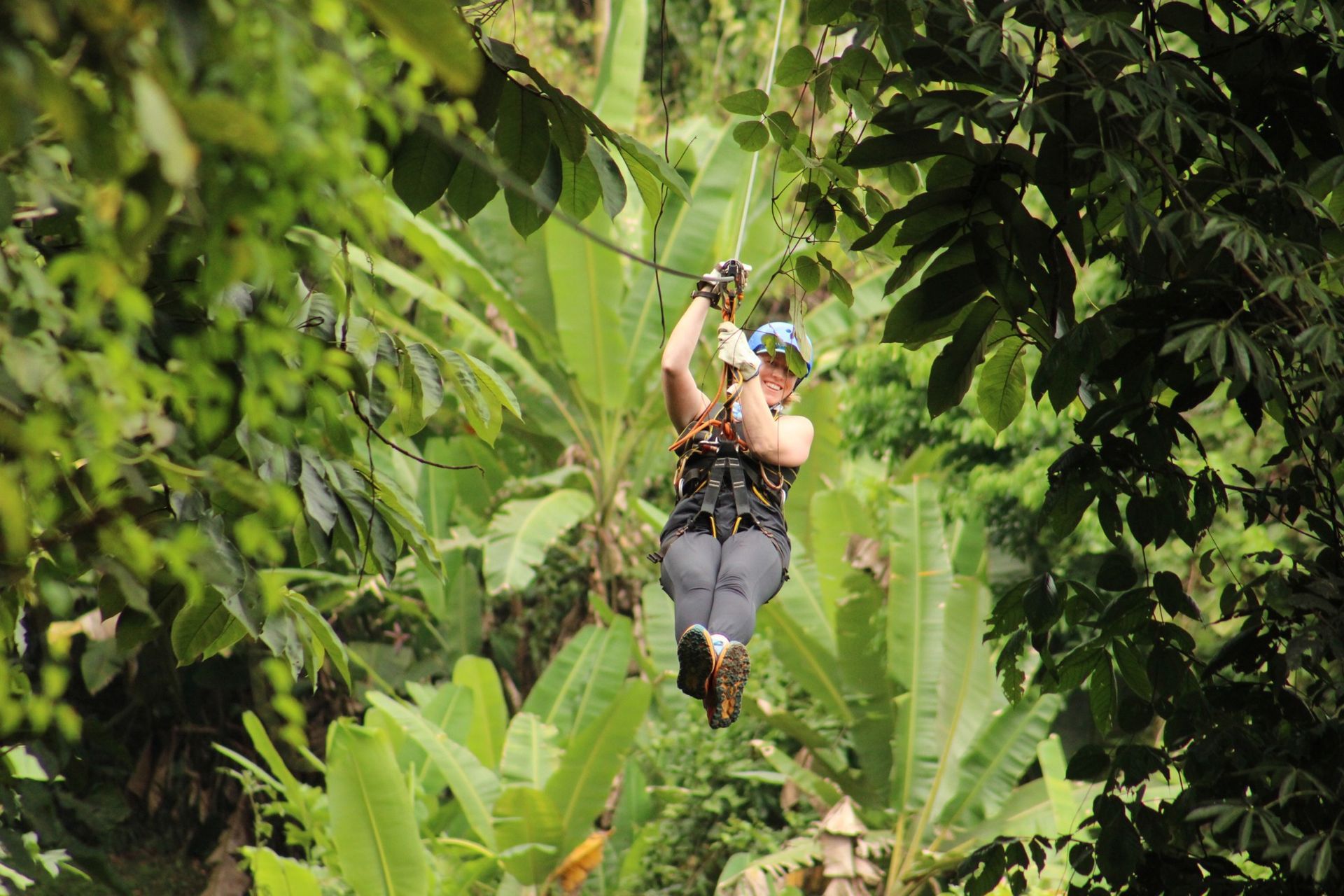 A woman is flying through the air on a zip line in the jungle.