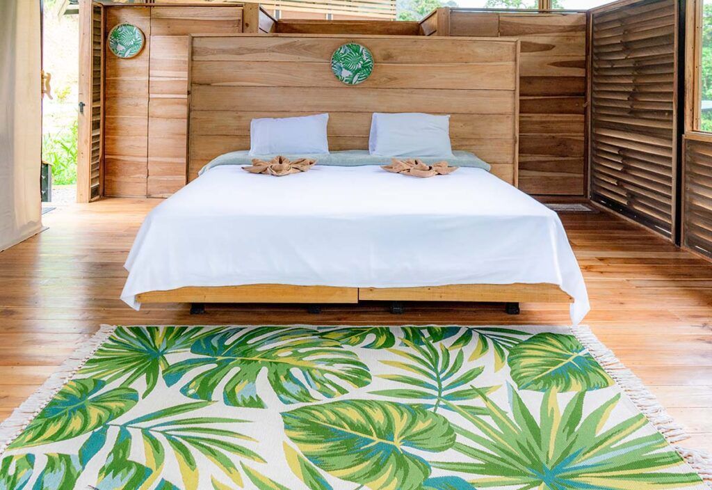 A bedroom with a bed and a rug with tropical leaves on it.