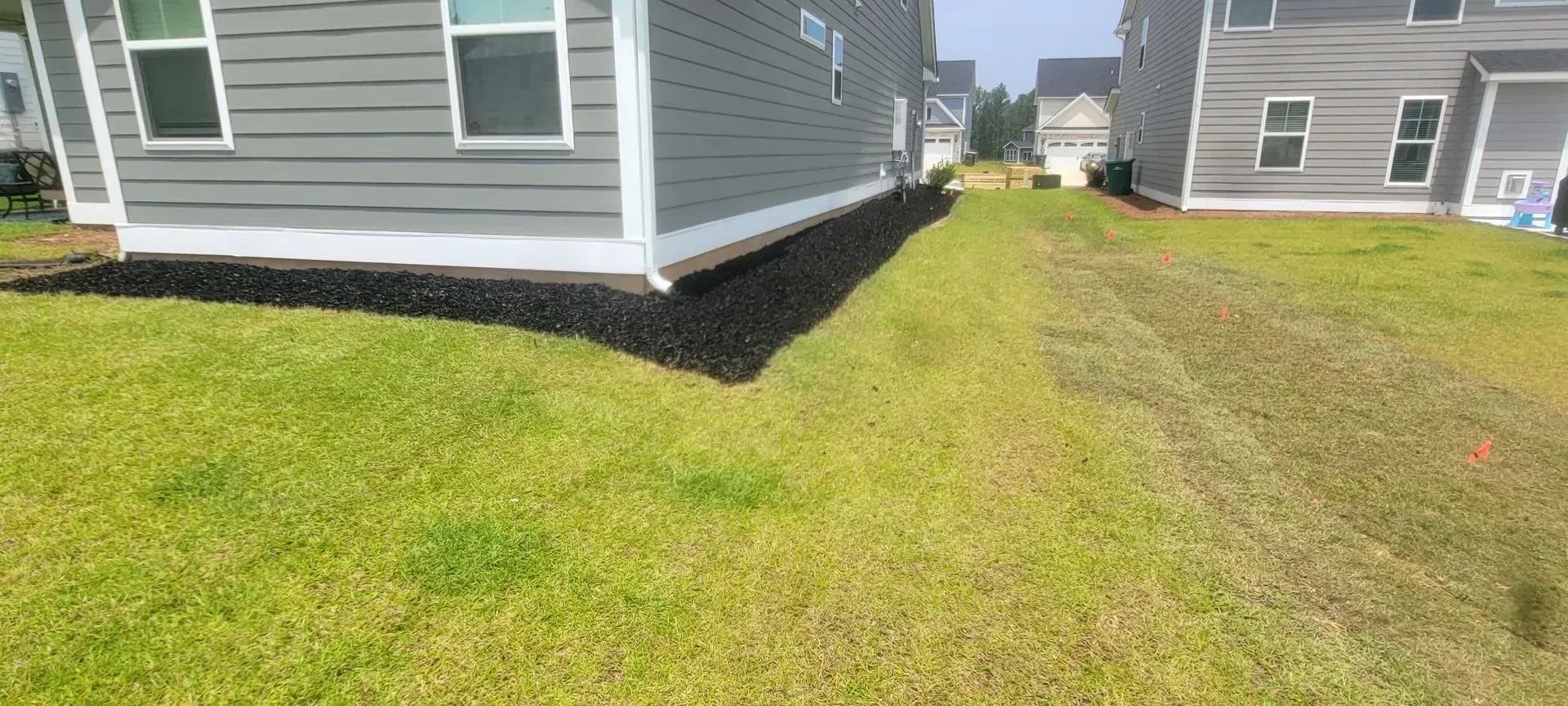 Side view of two-story gray houses with a grass yard and black mulch landscaping.