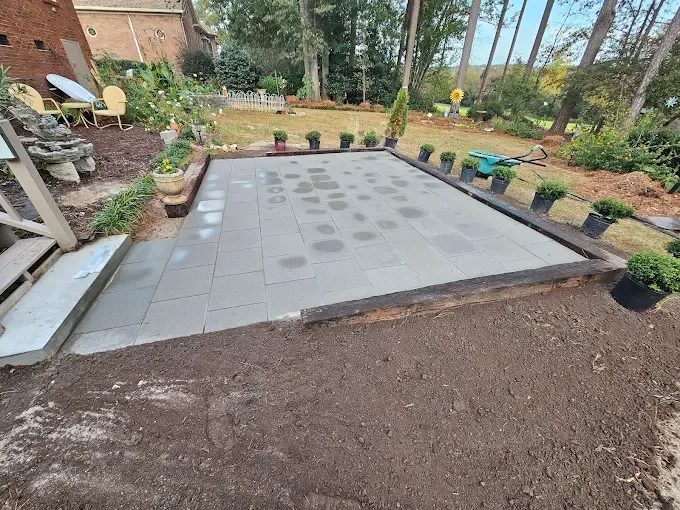 Finished patio with gray pavers and dark border, surrounded by soil and plants.