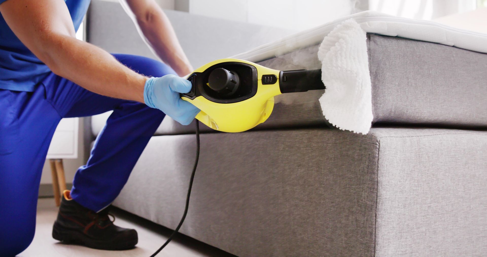 A man is cleaning a couch with a steam cleaner.
