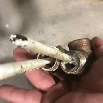 Hand holding a small, damaged copper pipe with three white objects inserted into it.